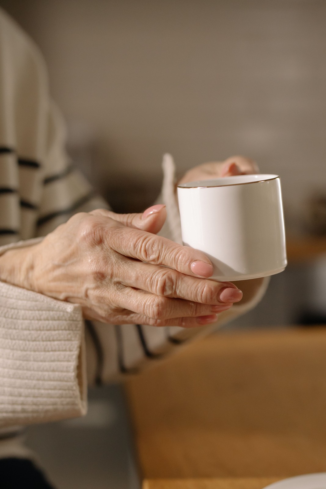 Hände um eine Kaffeetasse am Küchentisch im Morgenlicht